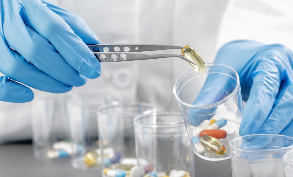 Sorting Medications. Doctor`s hand in blue gloves sorting with tweezers medication in glasses. Healthcare concept.